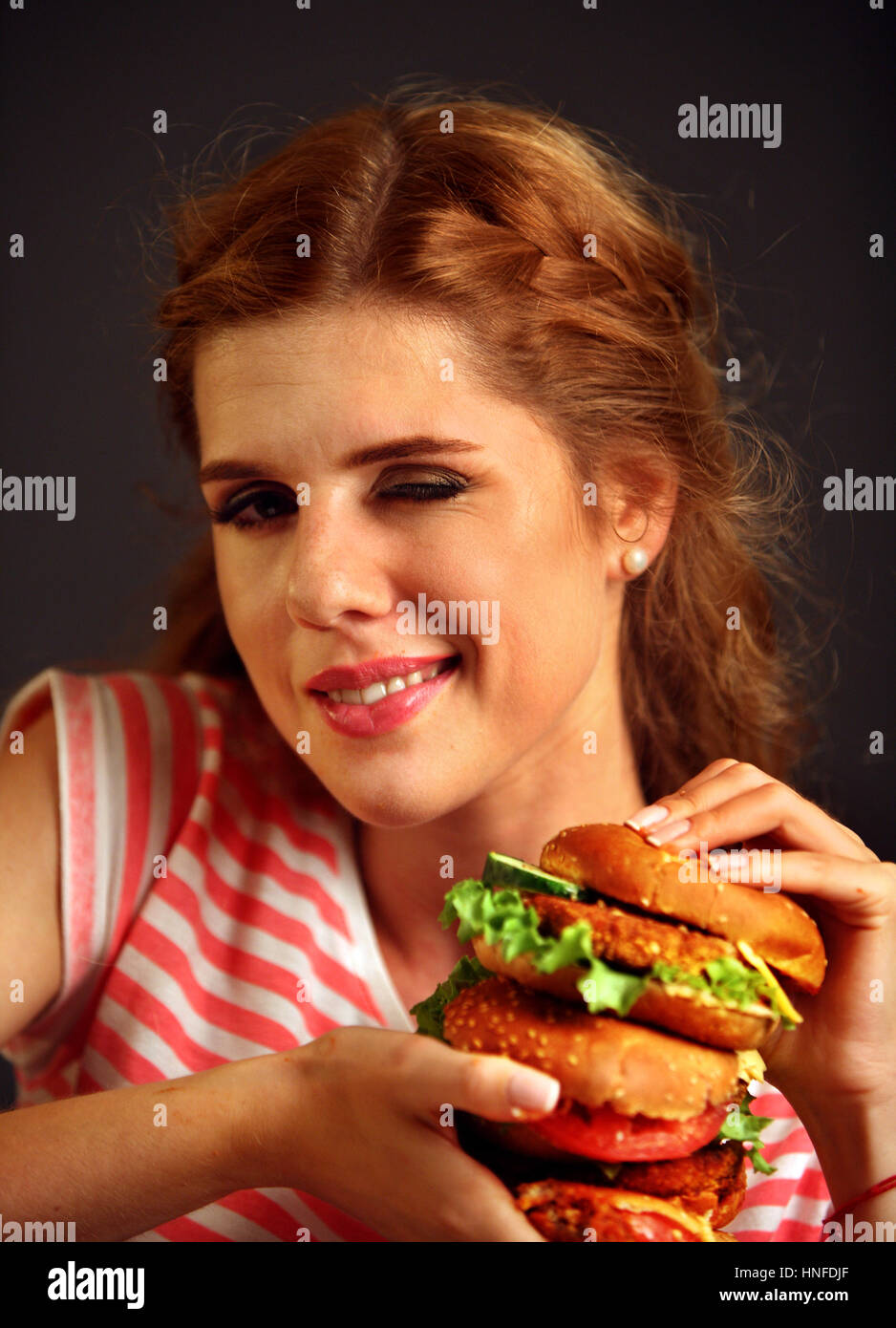 Donna di mangiare hamburger e winks. Felice studente sandwich di mangiare il pranzo. Foto Stock