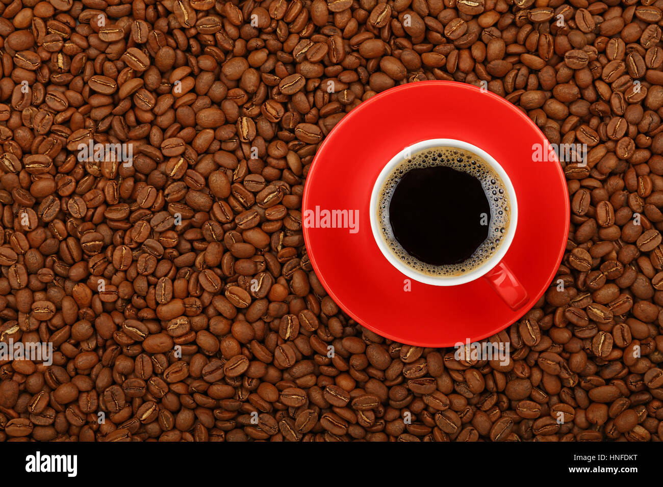 Piena Americano nero caffè filtrato in rosso tazza con piattino sullo sfondo di caffè torrefatto in grani, elevati vista superiore, vicino fino Foto Stock