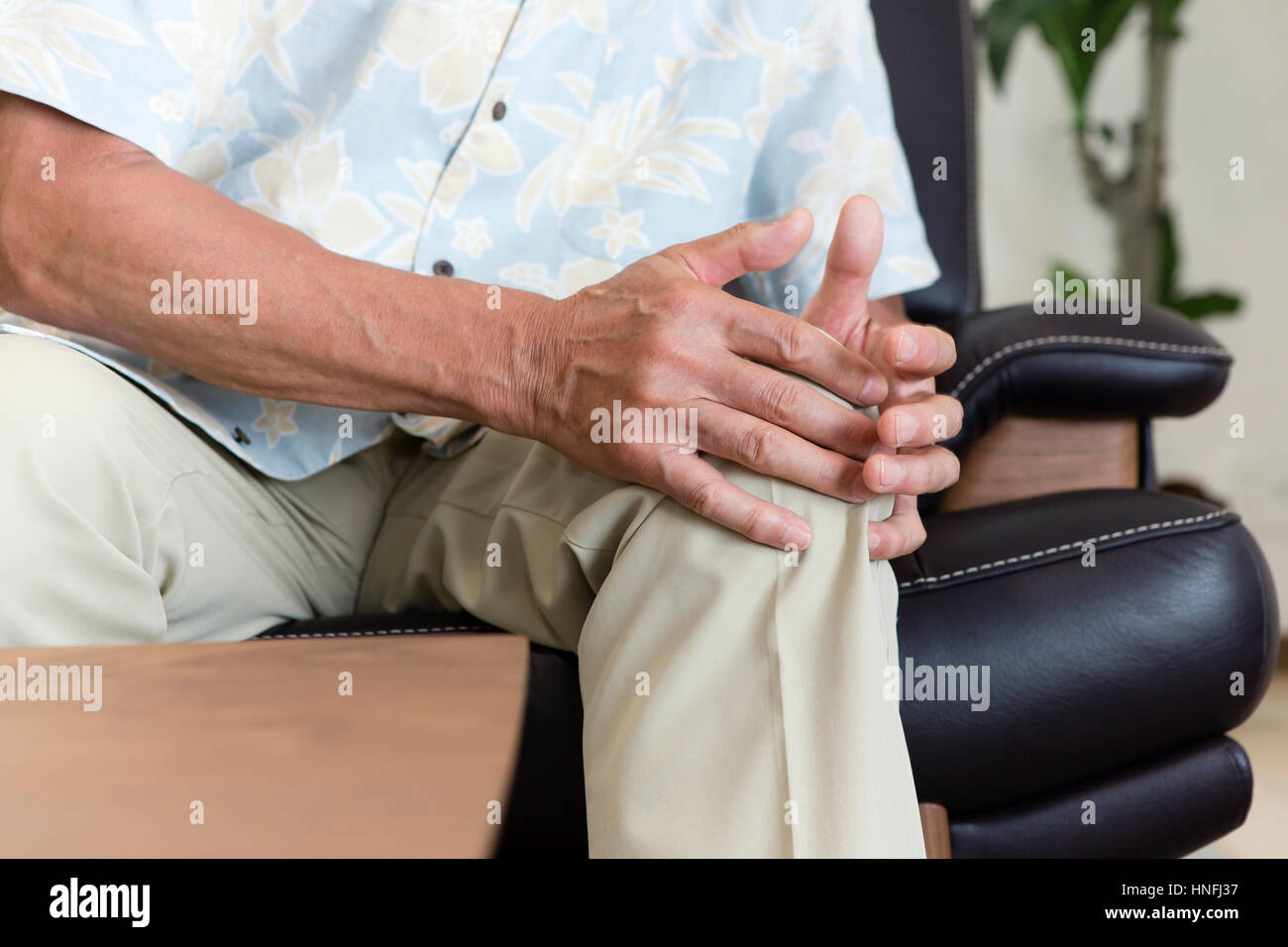 Un uomo anziano che copre la sua mano sulla sua genicula Foto Stock