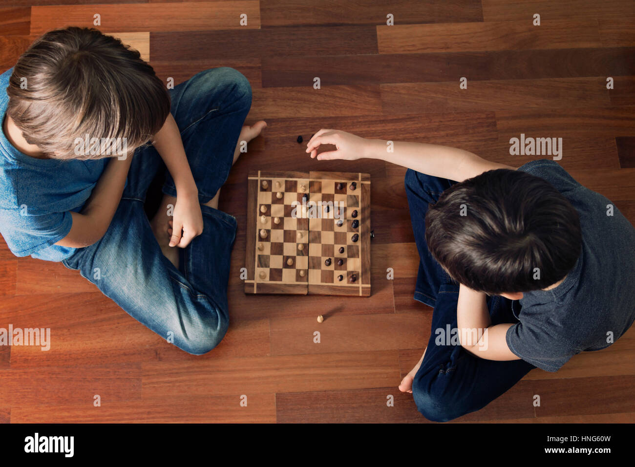 I bambini giocando a scacchi seduta sul pavimento in legno. Vista dall'alto. Gioco, istruzione, lifestyle, concetto di piacere. Immagine dai toni Foto Stock