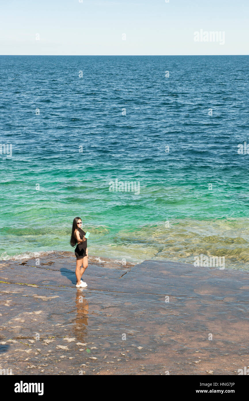 Asia femmina turistica prendendo un selfie con uno smartphone dal bordo del Lago Huron, Georgian Bay, Bruce Peninsula, Ontario, Canada. Foto Stock