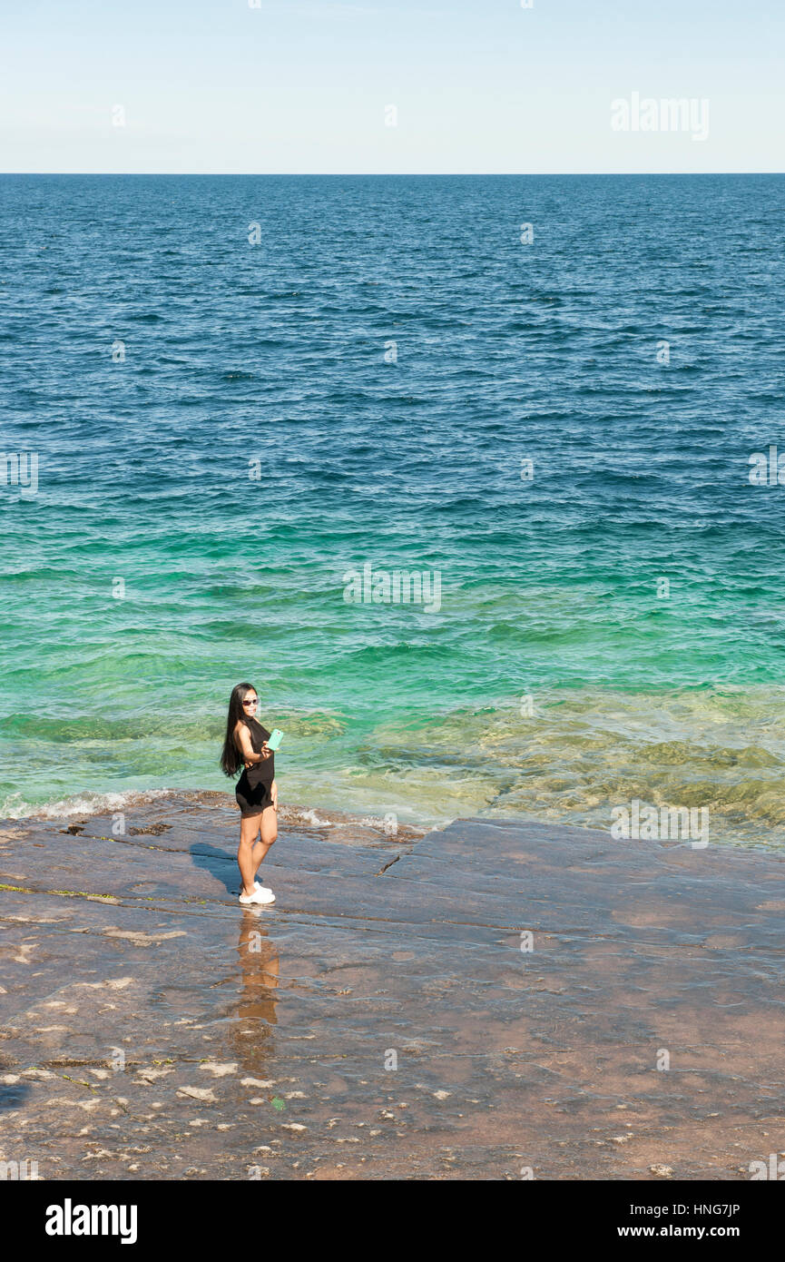Asia femmina turistica prendendo un selfie con uno smartphone dal bordo del Lago Huron, Georgian Bay, Bruce Peninsula, Ontario, Canada. Foto Stock