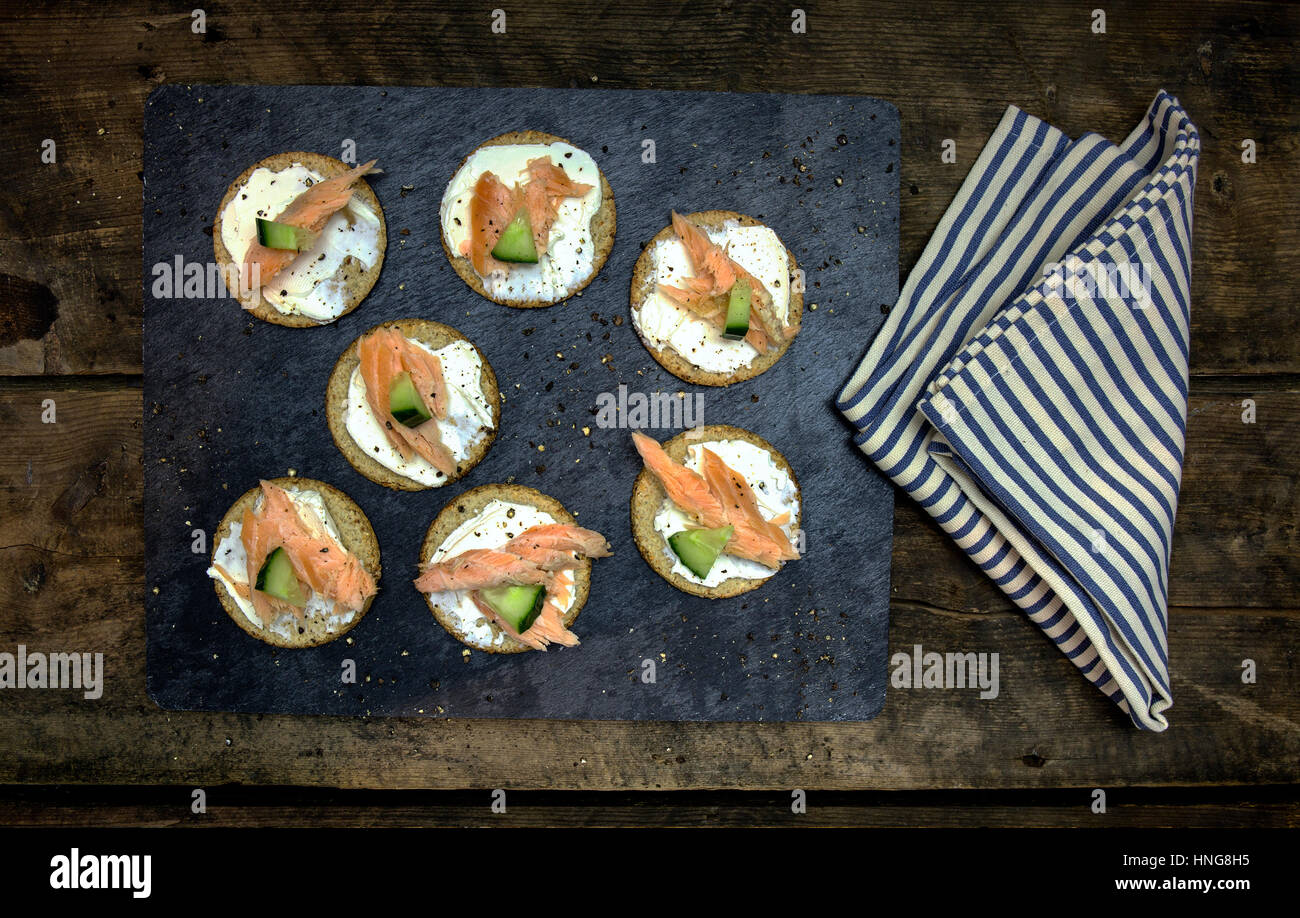 Torta di avena di cetriolo e tartine di salmone su un nero ardesia e rustico in legno scuro dello sfondo con pepe nero pestato e una a strisce blu igienico Foto Stock