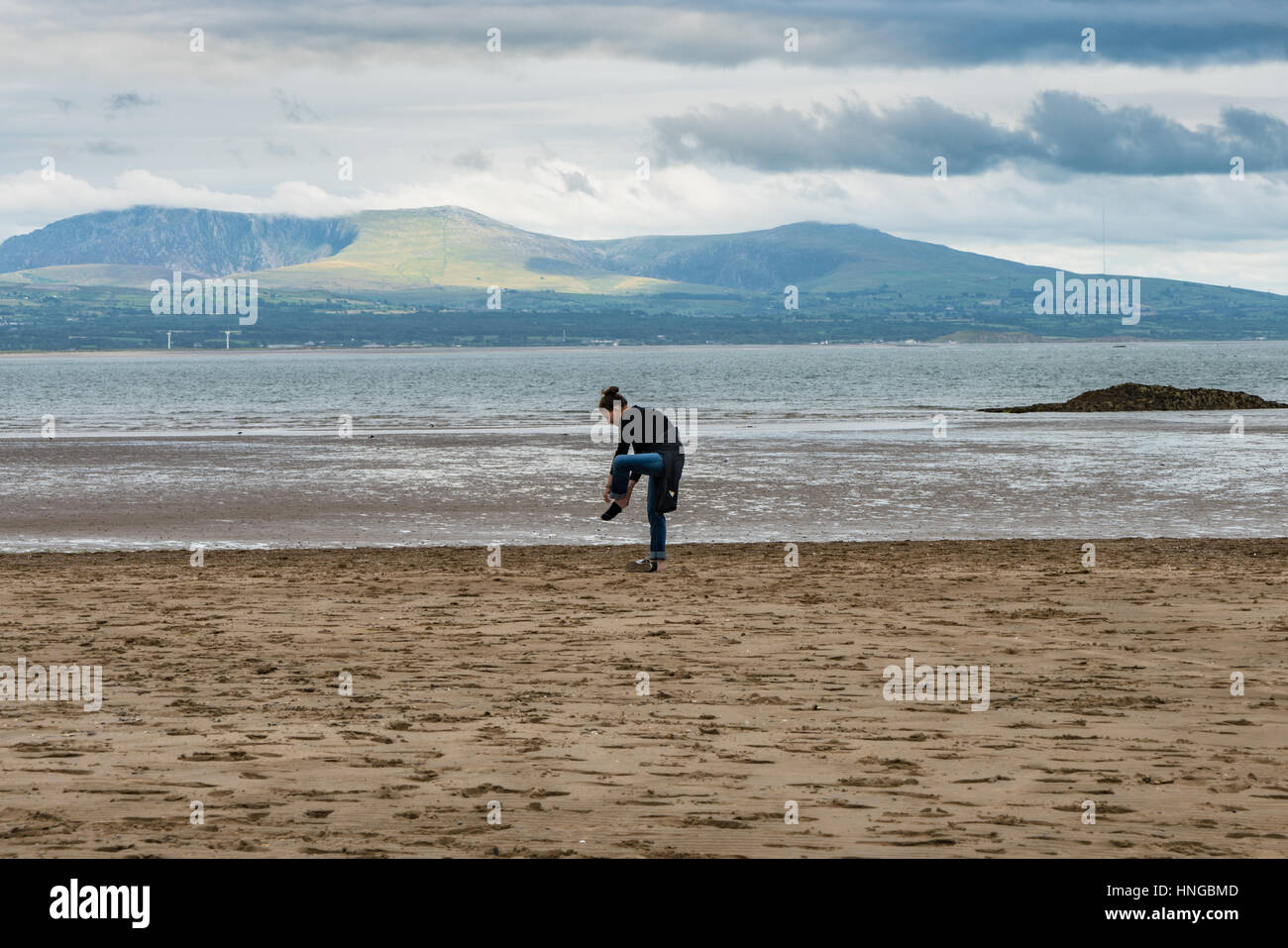 Signora decide a piedi nudi è meglio di scarpe di sabbia sulla spiaggia di Newborough Foto Stock
