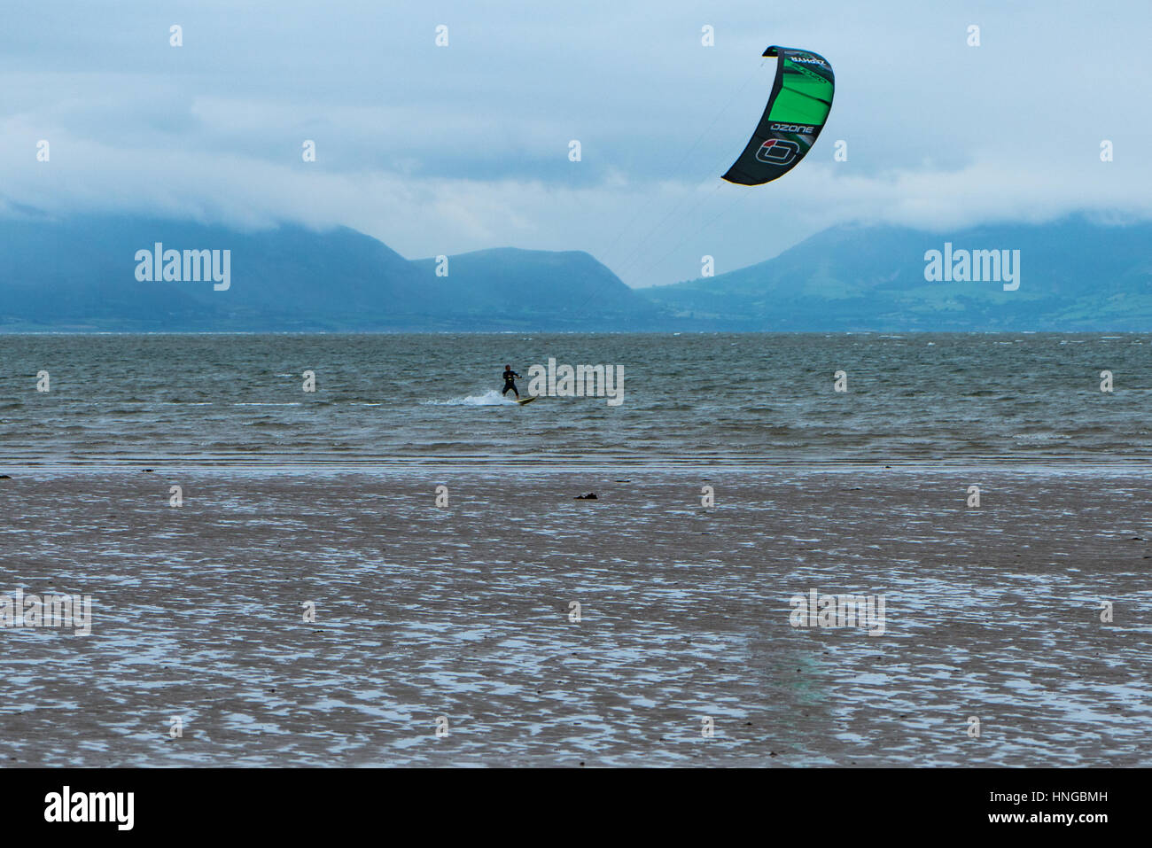 Un kite surfer off Newborough spiaggia con Snowdonia in background Foto Stock