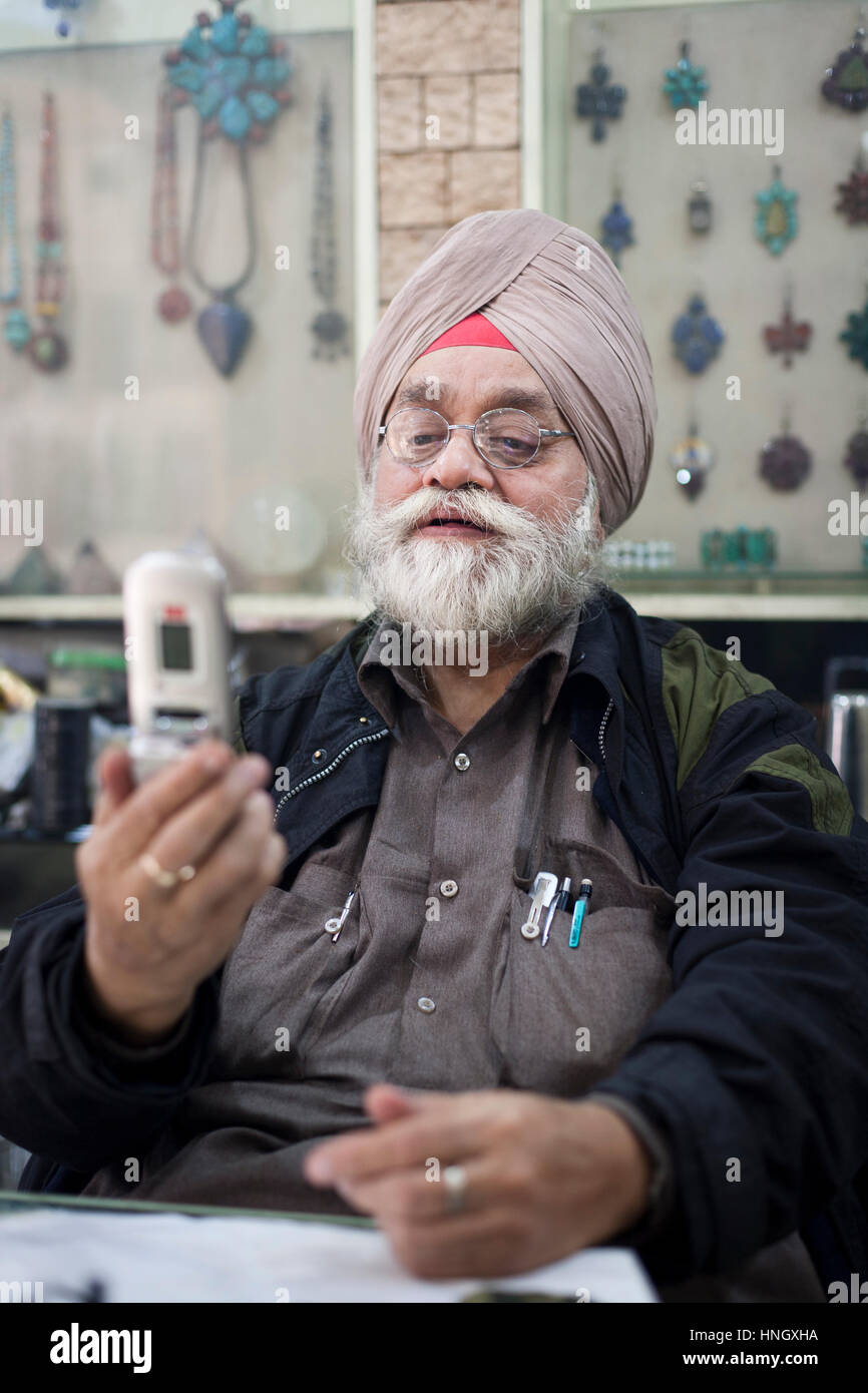 New Delhi, India - Febbraio, 16 2010: l'uomo che gestisce un negozio di posta indesiderata in Delhi ispezione di un telefono cellulare sta considerando l'acquisto. Foto Stock