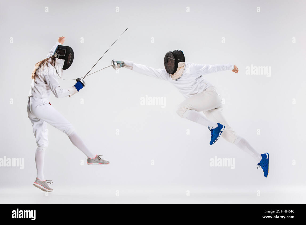 La donna e l uomo indossare tuta scherma la pratica con le spade contro il grigio di sfondo per studio Foto Stock