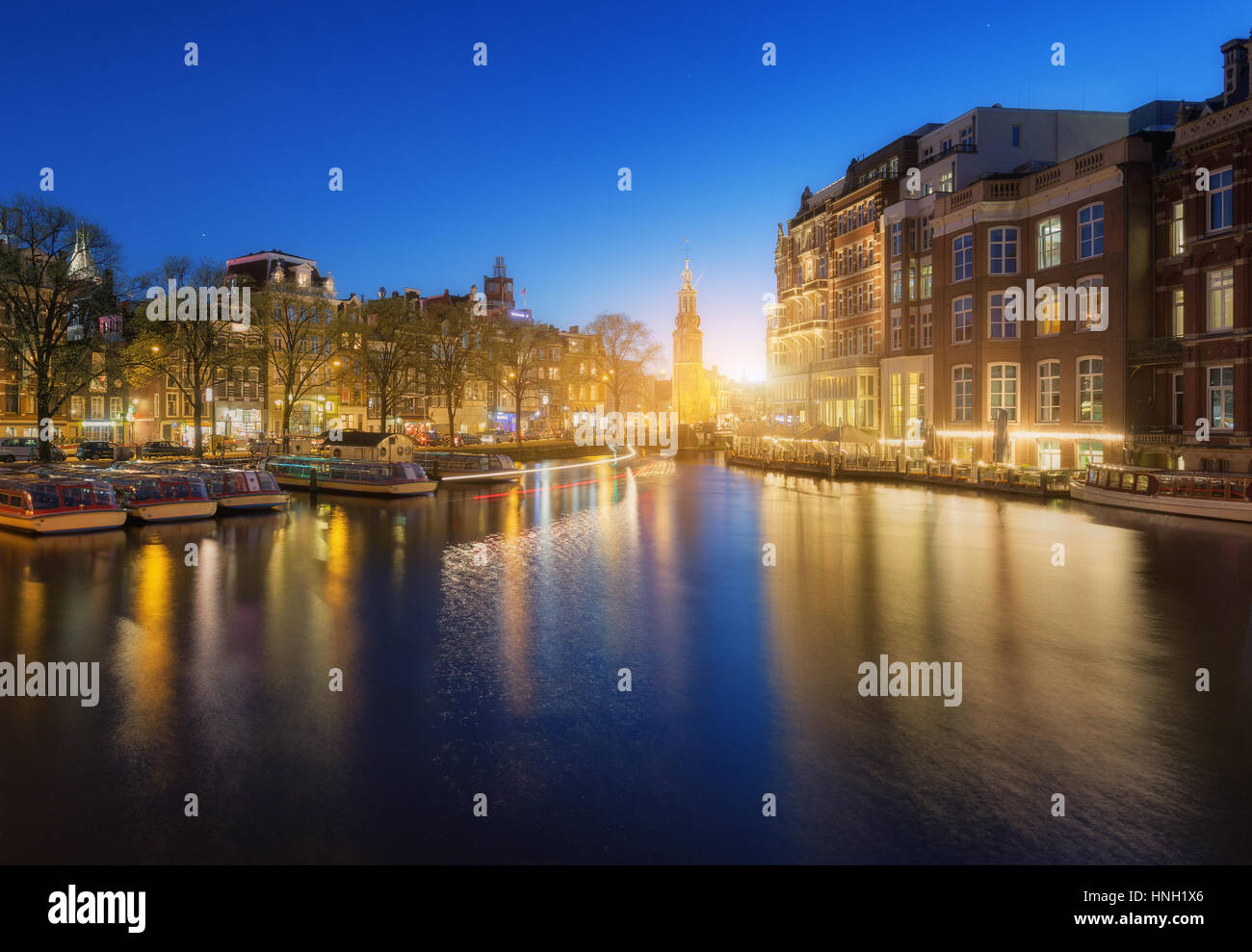 Colorato paesaggio al tramonto in Amsterdam, Paesi Bassi. Riflette le luci della città in acqua con il blu del cielo al crepuscolo. Illuminazione notturna degli edifici Foto Stock