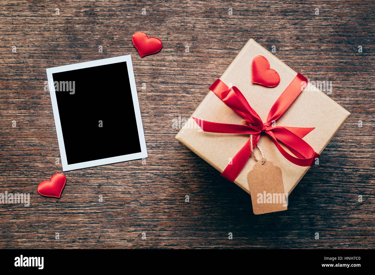 Blank photo frame e confezione regalo con cuore rosso su uno sfondo di legno. Foto Stock