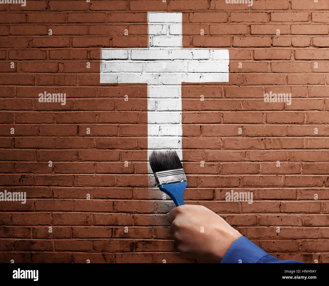 Persone mano con pennello per rendere la croce bianca forma sulla parete di mattoni Foto Stock