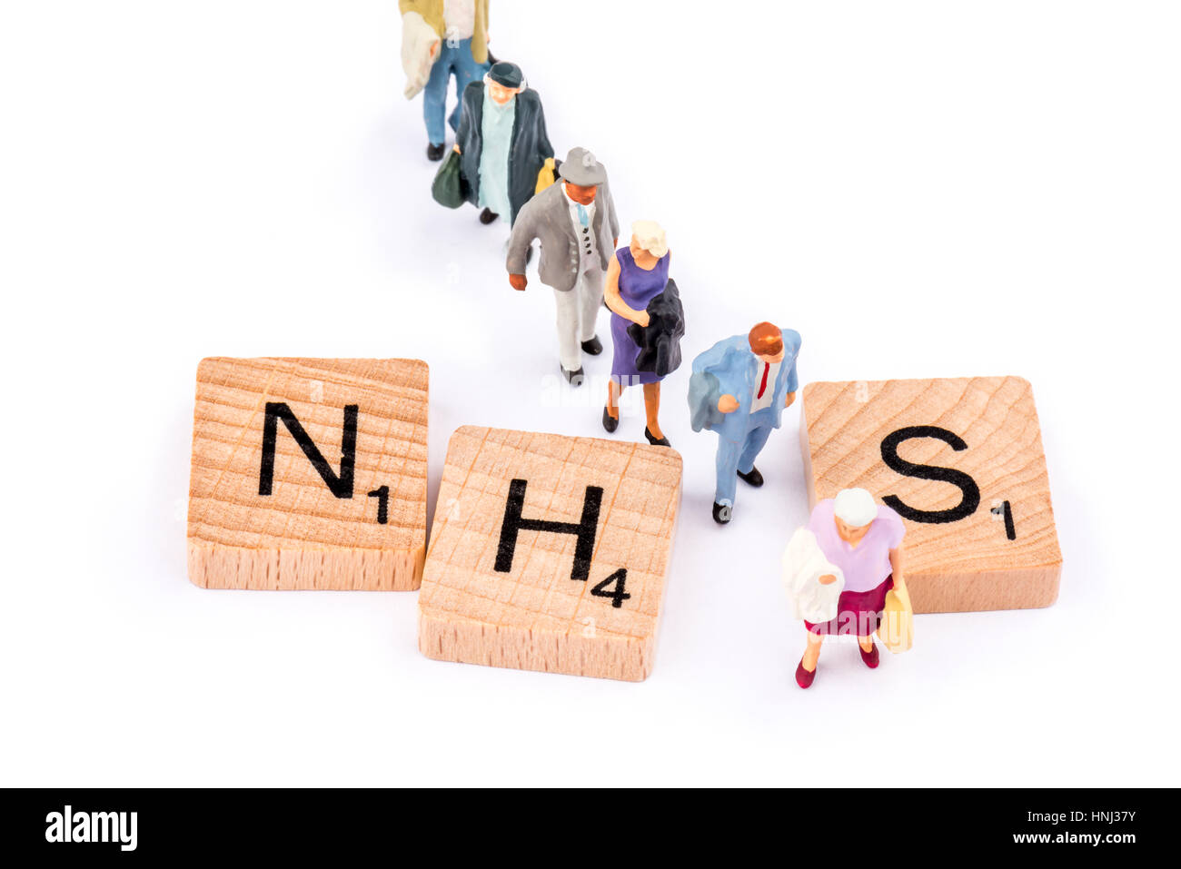 Scrabble lettere costituiscono la parola NHS. Una linea di persone a piedi tra le lettere H e S. Foto Stock