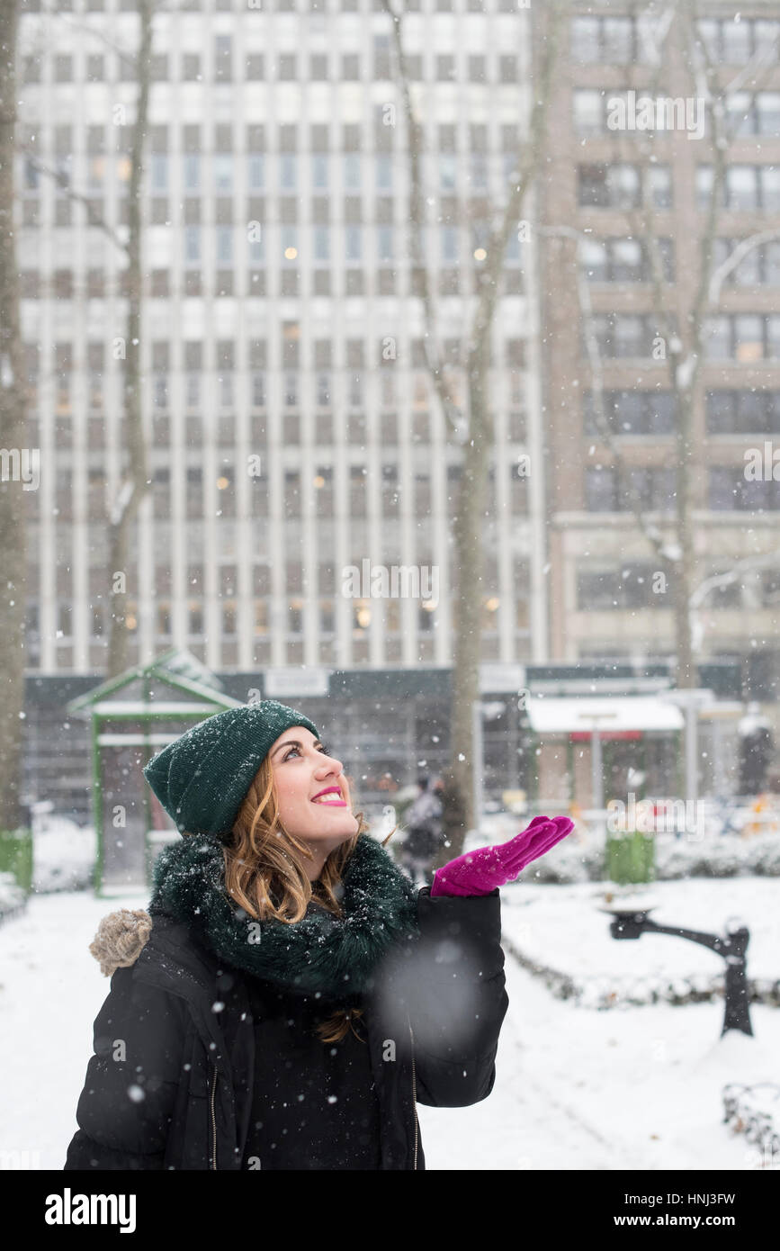 Donna sorridente godendo di nevicare mentre in piedi in città Foto Stock