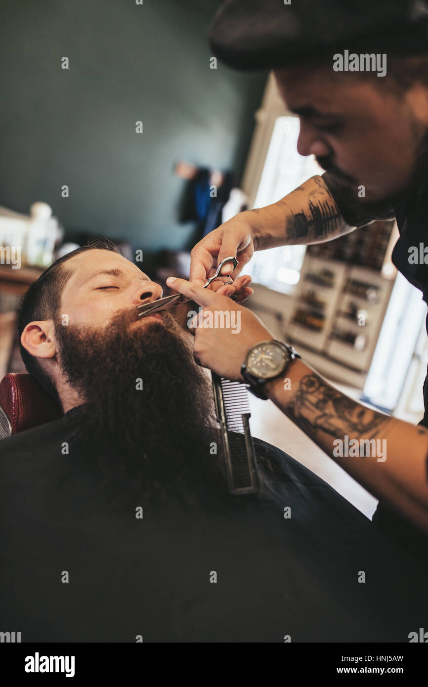 Professional barbiere di rifilatura dei baffi del cliente nel suo salone. L'uomo ottenendo la sua barba rasata in un salone. Foto Stock