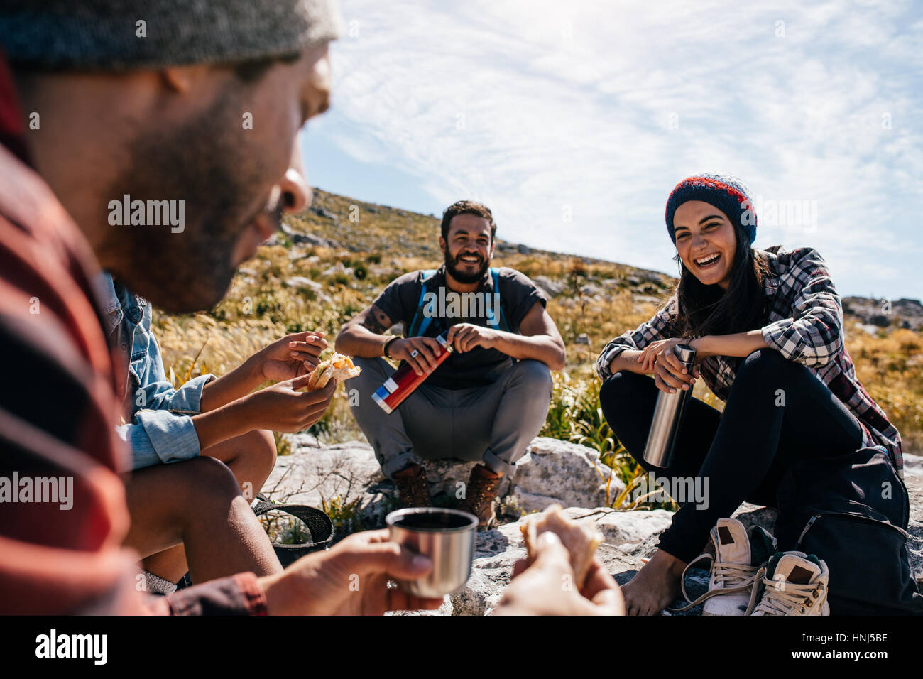 Gruppo di persone rilassarsi e mangiare durante l'escursione. Giovane donna con amici prendendo una pausa durante una passeggiata in campagna. Foto Stock