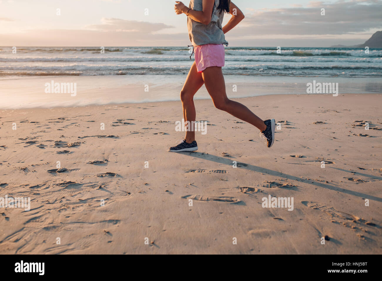 Sezione bassa colpo di giovane donna jogging sulla spiaggia. Femmina Fitness sulla corsa mattutina a riva del mare, concentrarsi sui piedi. Foto Stock