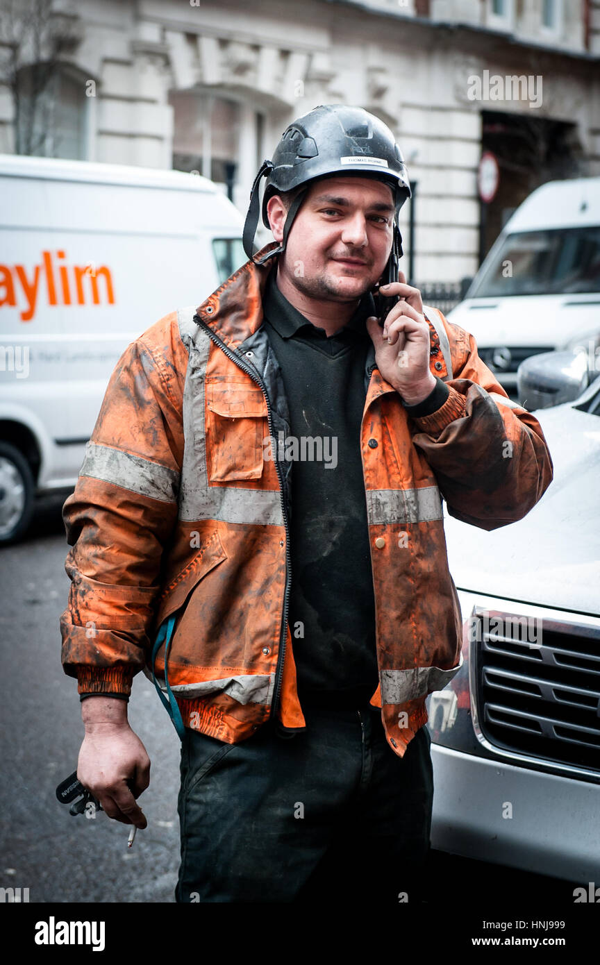 Workman con vestiti sporchi sul telefono con cirgarette Foto Stock