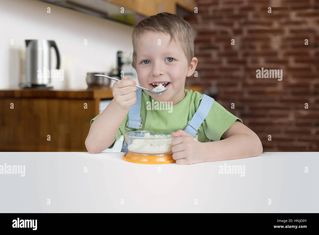 Cinque anni ragazzo mangia il porridge in cucina Foto Stock