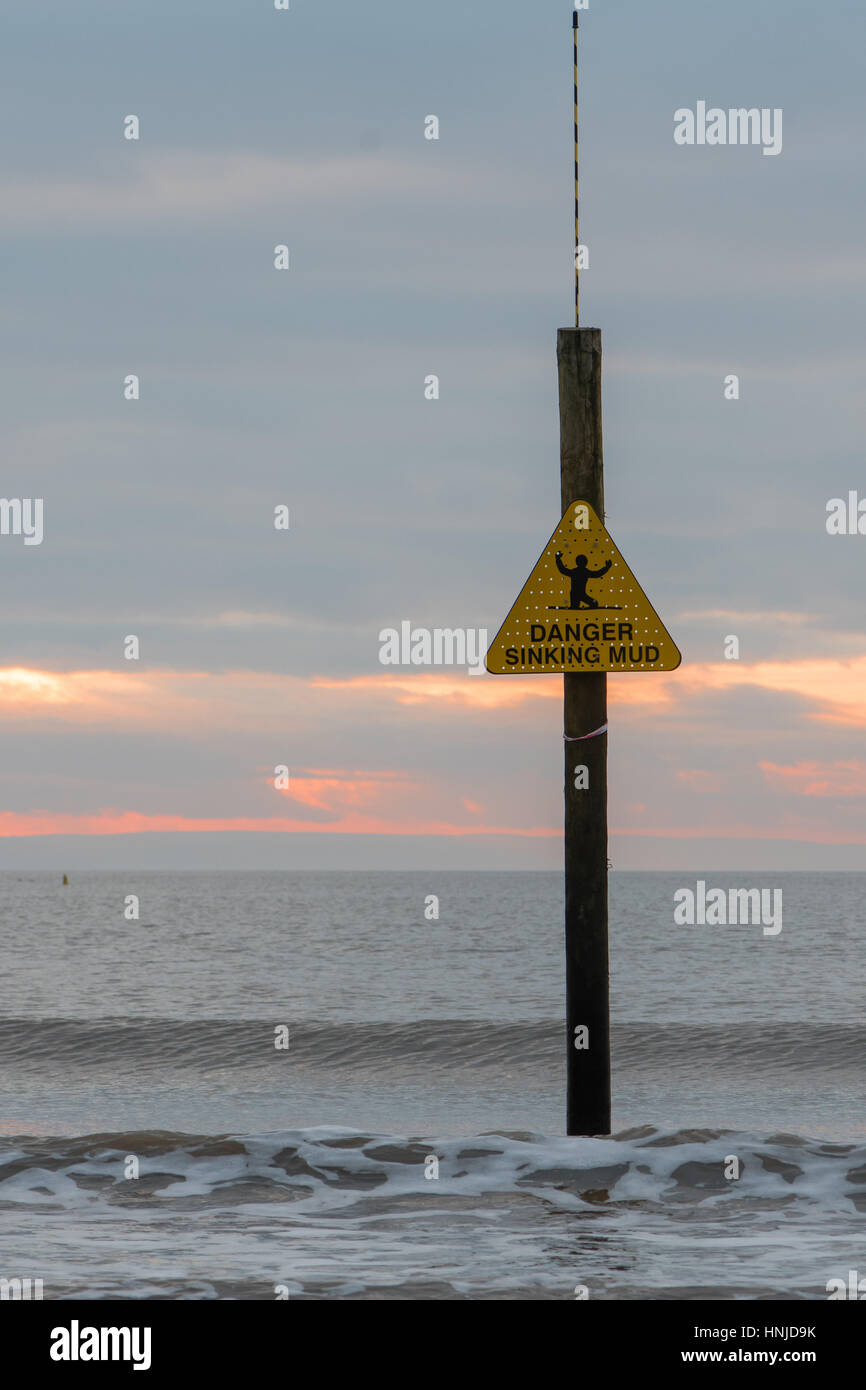 Pericolo di affondamento segno di fango nella parte anteriore delle onde e il tramonto. Avvertimento del litorale pericolose a Weston-super-Mare, Somerset, Regno Unito, con marea Foto Stock