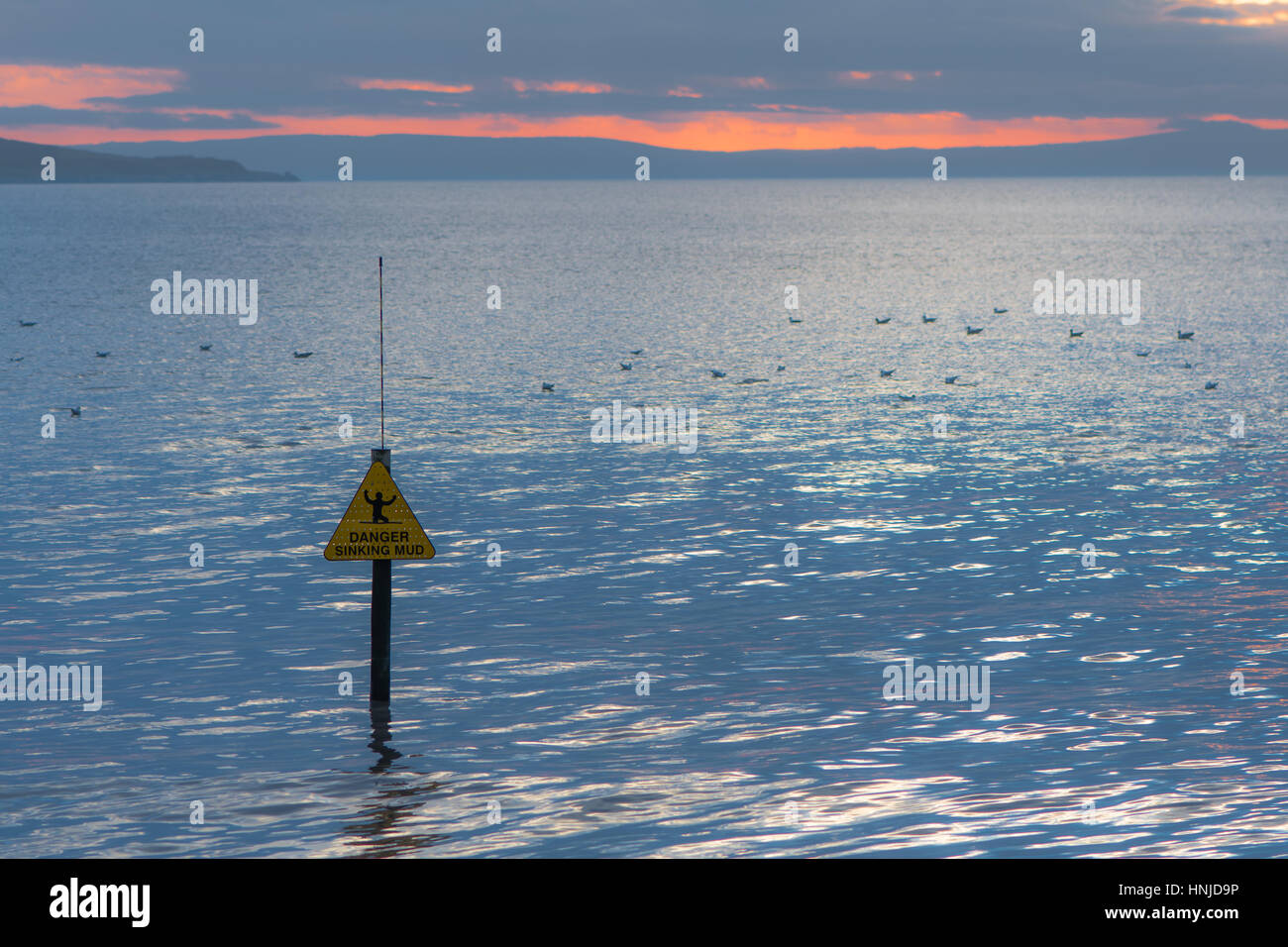 Pericolo di affondamento segno di fango di fronte al mare e al tramonto. Avvertimento del litorale pericolose a Weston-super-Mare, Somerset, Regno Unito, con Brean giù e gabbiani Foto Stock