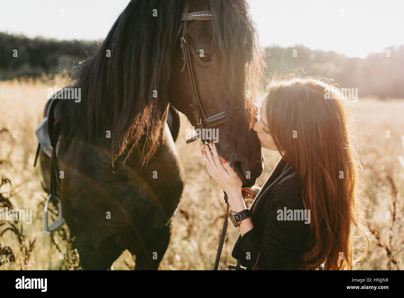 Caucasian giovane donna che indossa abiti neri, baciando il suo cavallo nero Foto Stock