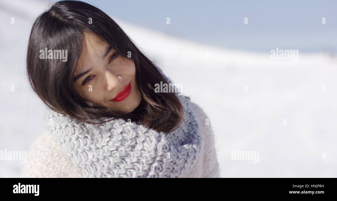 Felice carina ragazza asiatica godendo le vacanze inverno tempo. Sorride alla telecamera con il rossetto rosso sulle labbra. Indossare caldo scard di lana e un maglione. Foto Stock