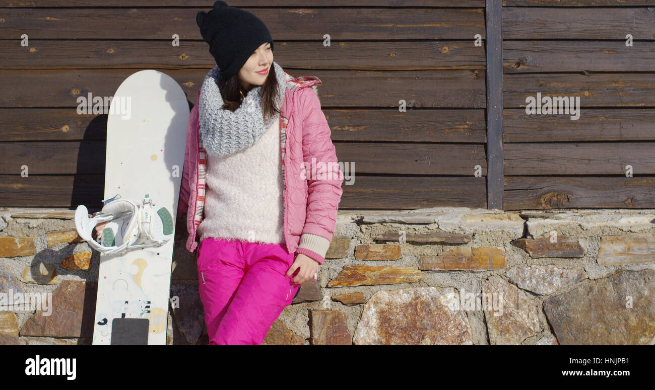 Tre quarti di corpo ritratto di attraente giovane donna in rosa doposci  sorridente con lo snowboard edificio di legno in background Foto stock -  Alamy