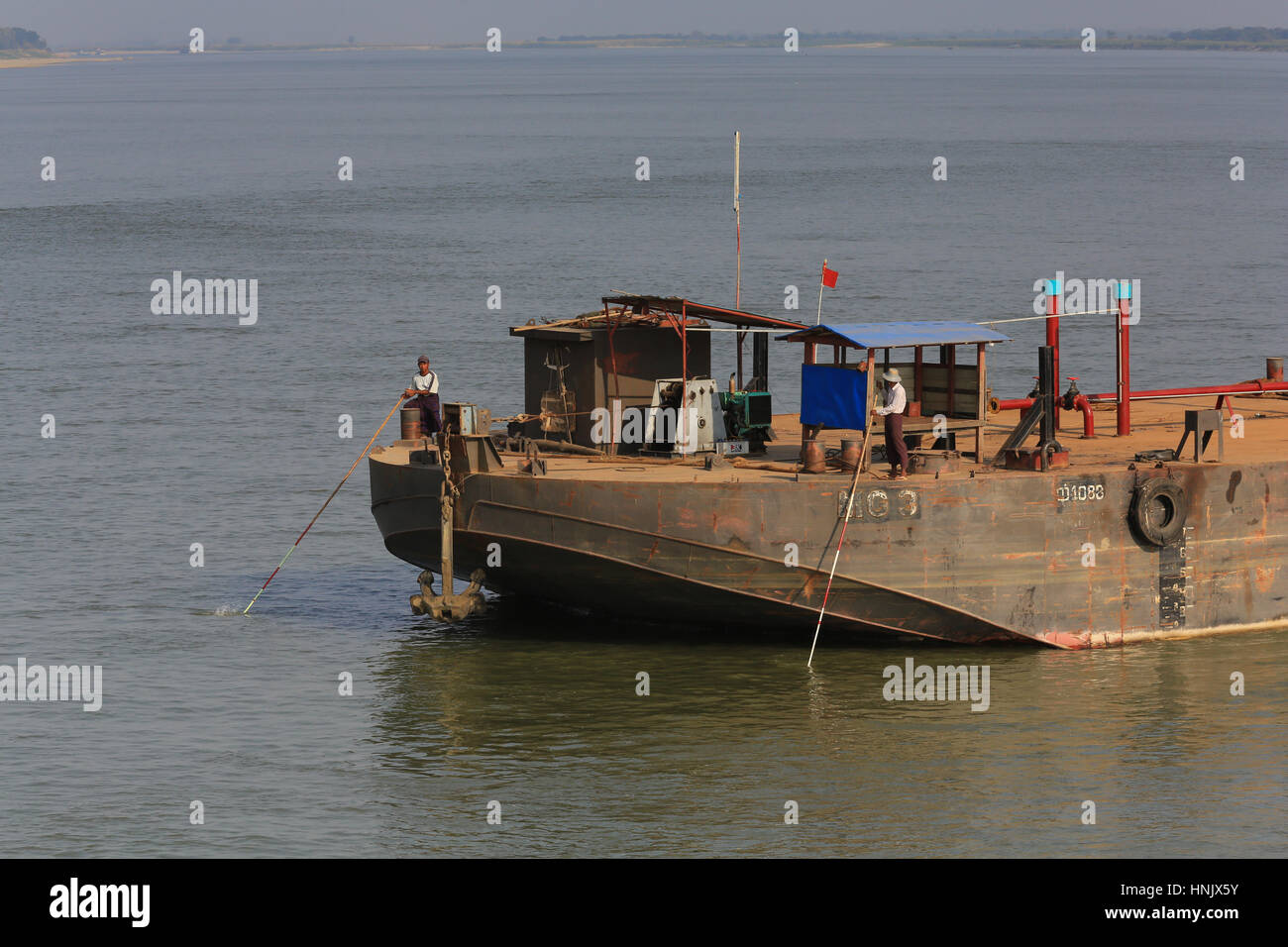 Barge equipaggio sono usando poli lunghi per suonare la profondità dell'acqua sul fiume Irrawaddy, Sagaing Regione, Myanmar (Birmania). Foto Stock