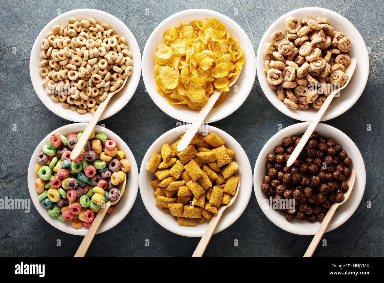 Varietà di cereali freddi in bianco ciotole con cucchiai di legno, veloce colazione per bambini Foto Stock