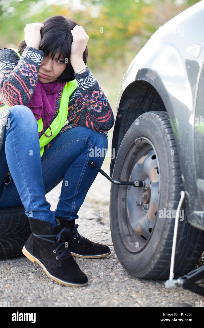 La donna la sostituzione di una ruota su un auto sulla strada vuota, messa a fuoco selettiva e piccole profondità di campo Foto Stock