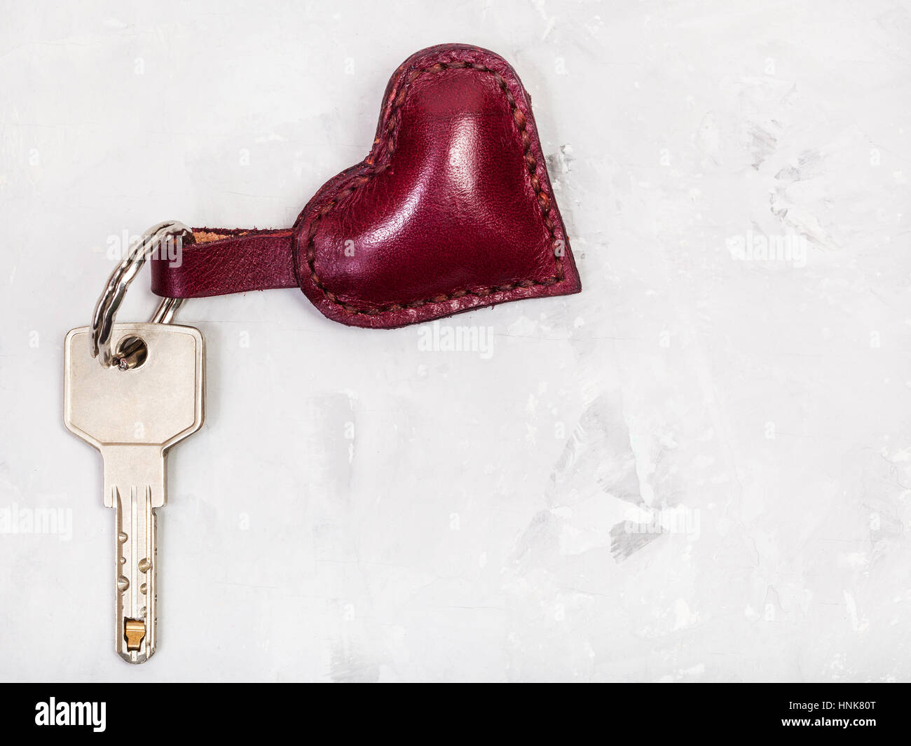 Chiave apertura porta con pelle di colore rosso forma di cuore portachiavi su piastra in calcestruzzo Foto Stock