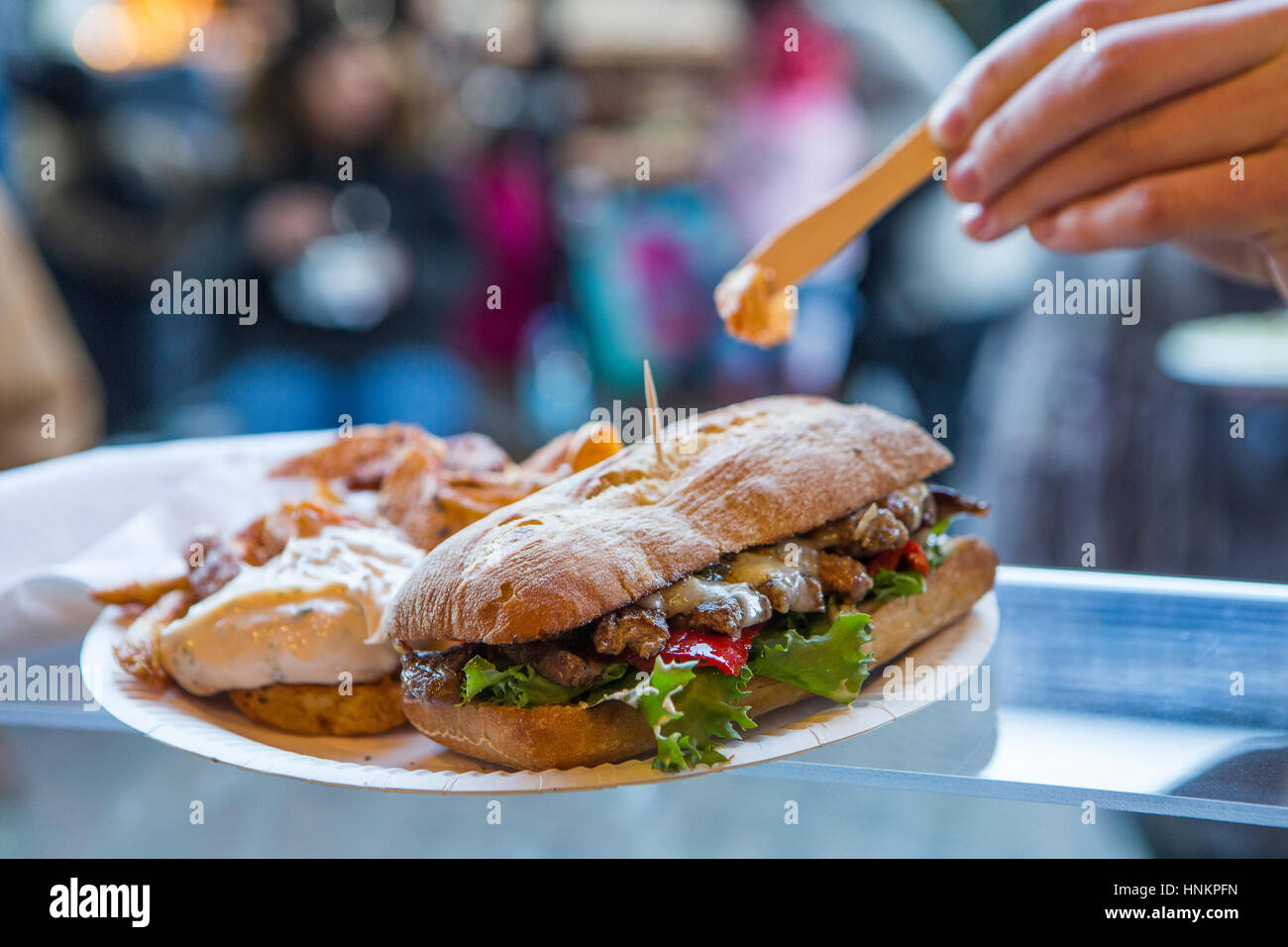Steak sandwich ciabatta con patate fritte street food con mano femmina indossando festival braccialetti chip di immersione nella maionese. Foto Stock