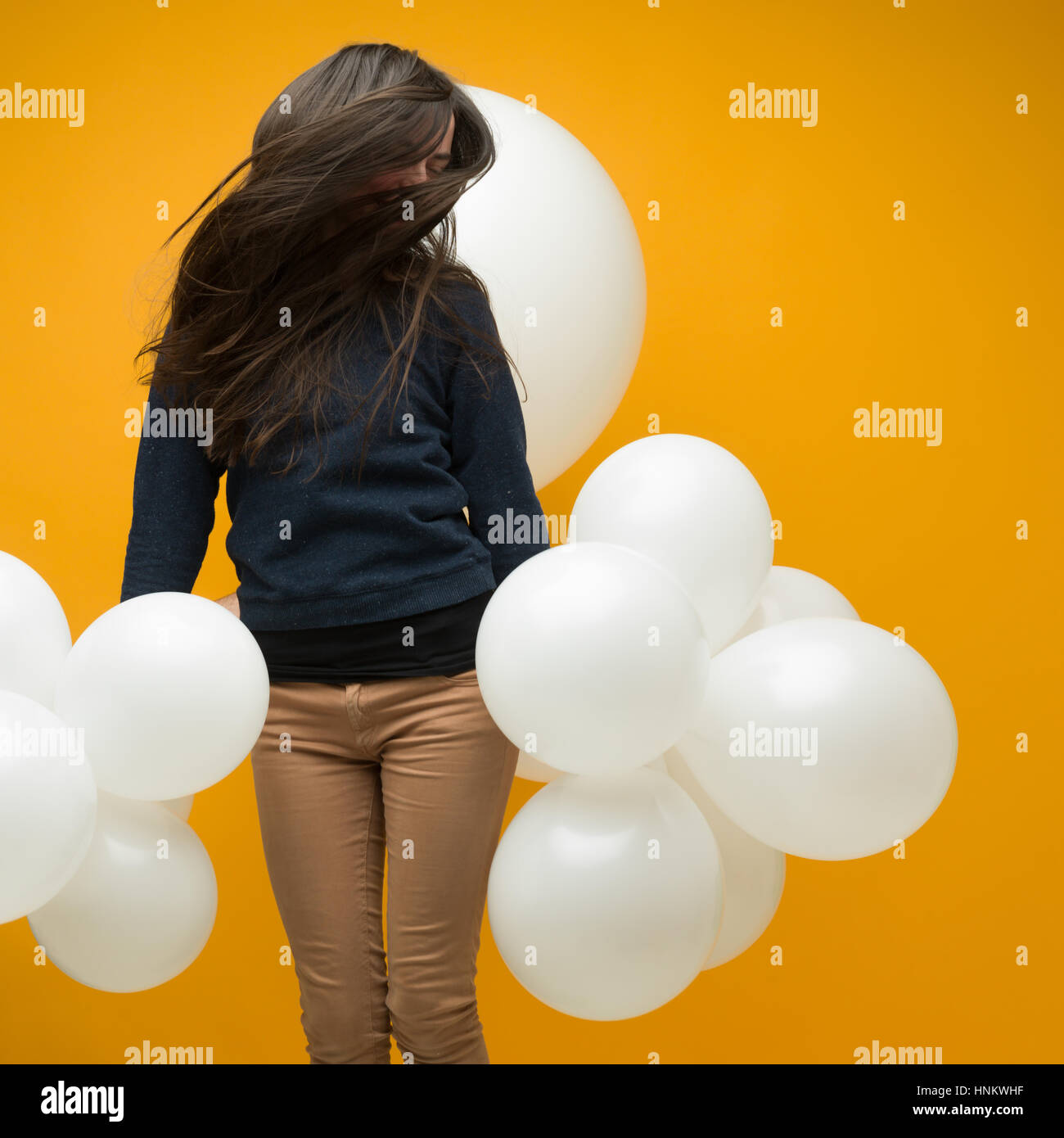 Bruna giovane donna con capelli lunghi danceing con palloncini bianchi nelle sue mani su sfondo giallo Foto Stock