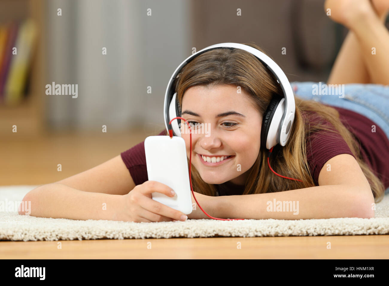 Felice teen la visione di contenuti multimediali on line in uno smartphone giacente su un tappeto sul pavimento del salotto di casa Foto Stock