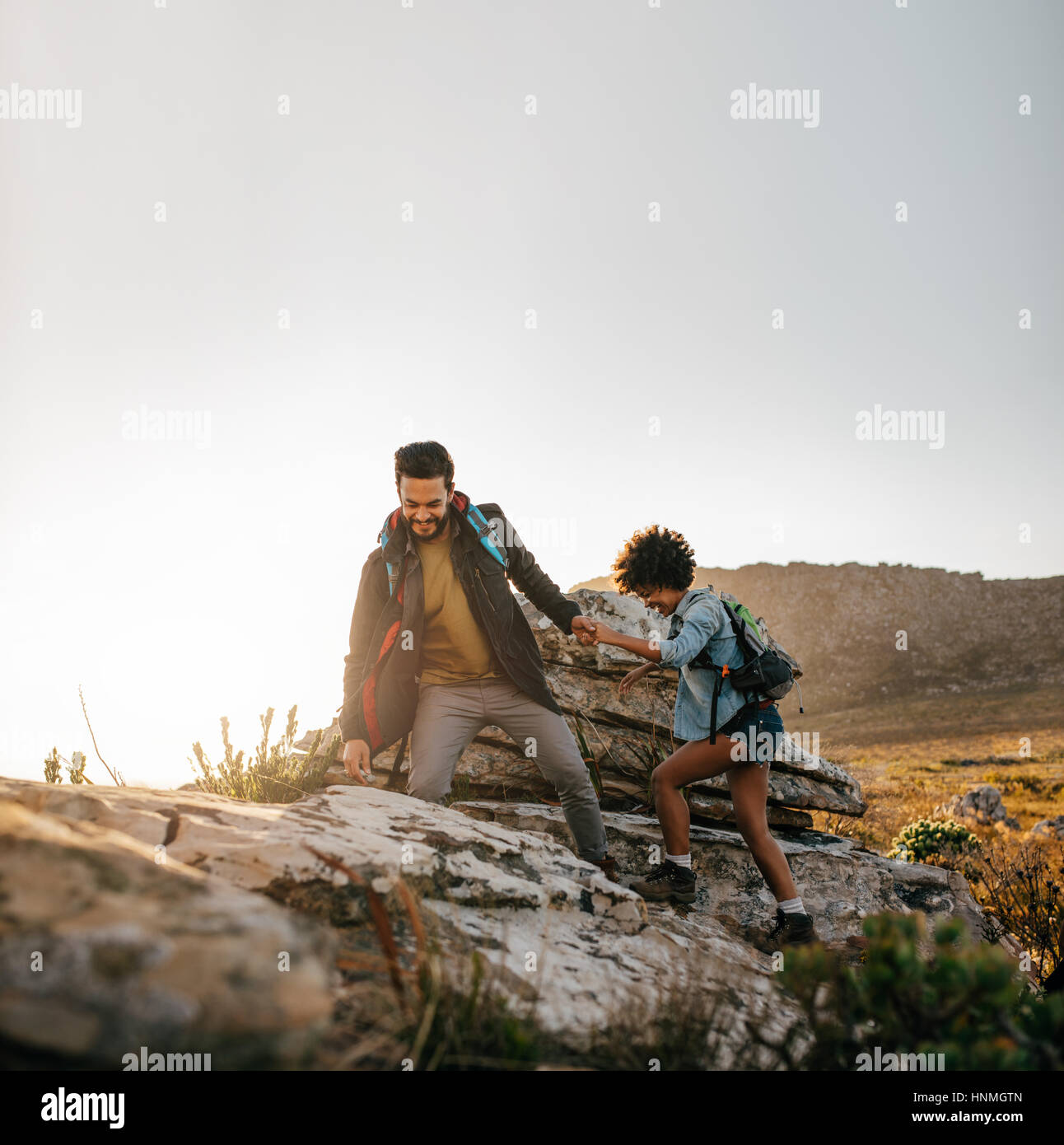 Coppia giovane escursionismo si aiutano a vicenda in montagna. Giovane maschio escursionista aiutando amico femmina durante il trekking in montagna. Foto Stock