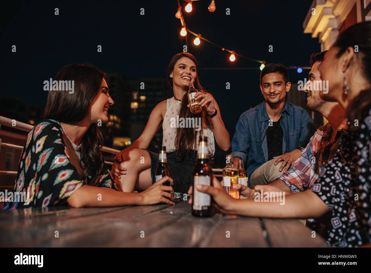 Un gruppo di giovani felici hanno avente un tetto partito alla sera. Gli amici sorseggiando party con bevande. Foto Stock Un gruppo di giovani felici hanno avente un tetto partito alla sera. Gli amici sorseggiando party con bevande. Foto Stock