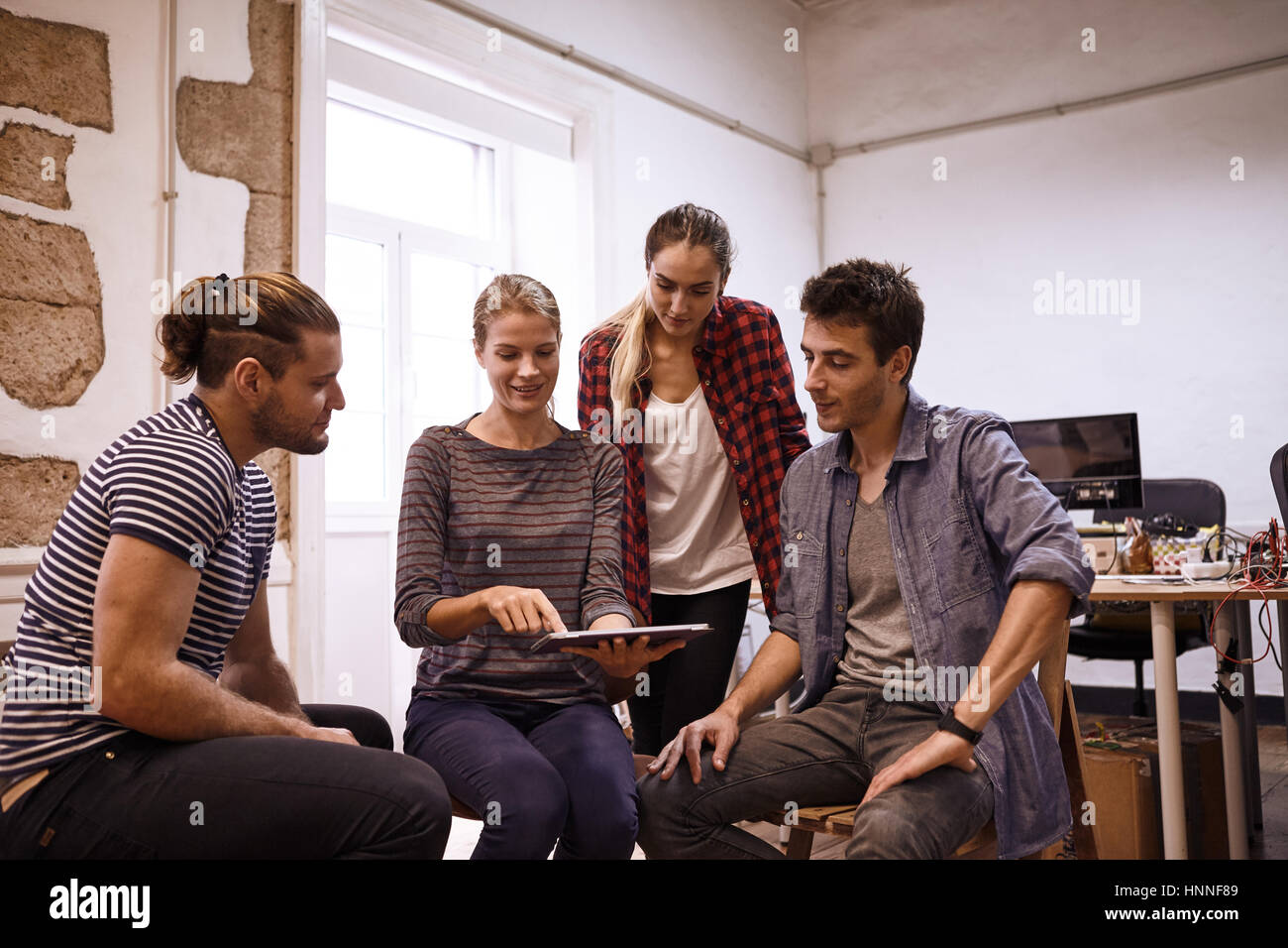 Young business team seduti e in piedi intorno a semi cerchio per condividere pensieri e idee intorno a un nuovo concetto per il loro business Foto Stock