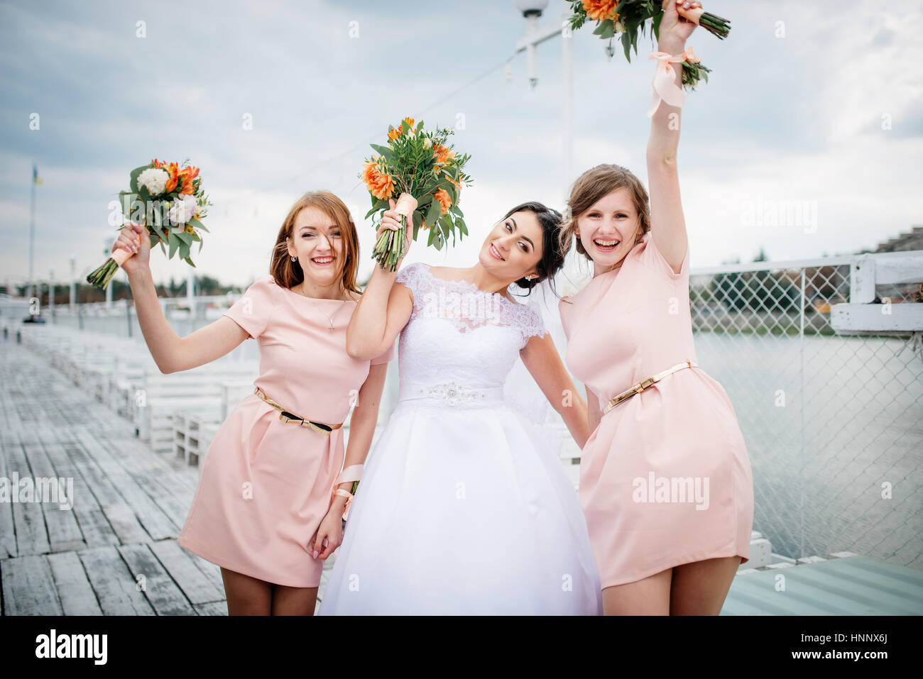 Sposa con bridesmaids poste sul molo di attracco a nuvoloso giorno di nozze. Foto Stock
