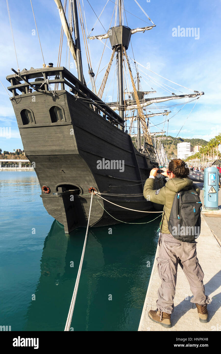 Giovane uomo che fa foto con il telefono cellulare della replica del vecchio galeone spagnolo, Nao Victoria, nave nel porto di Malaga. Foto Stock