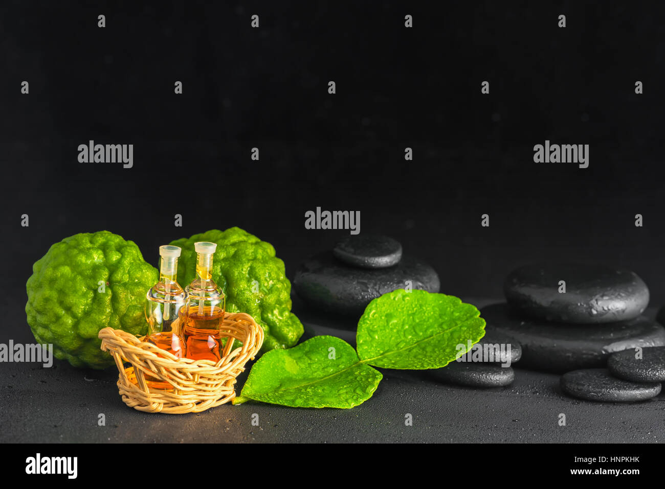 Concetto aromatico di bergamotto, foglia, olio profumato e zen pietre di basalto con gocce d'acqua su sfondo nero, close up Foto Stock