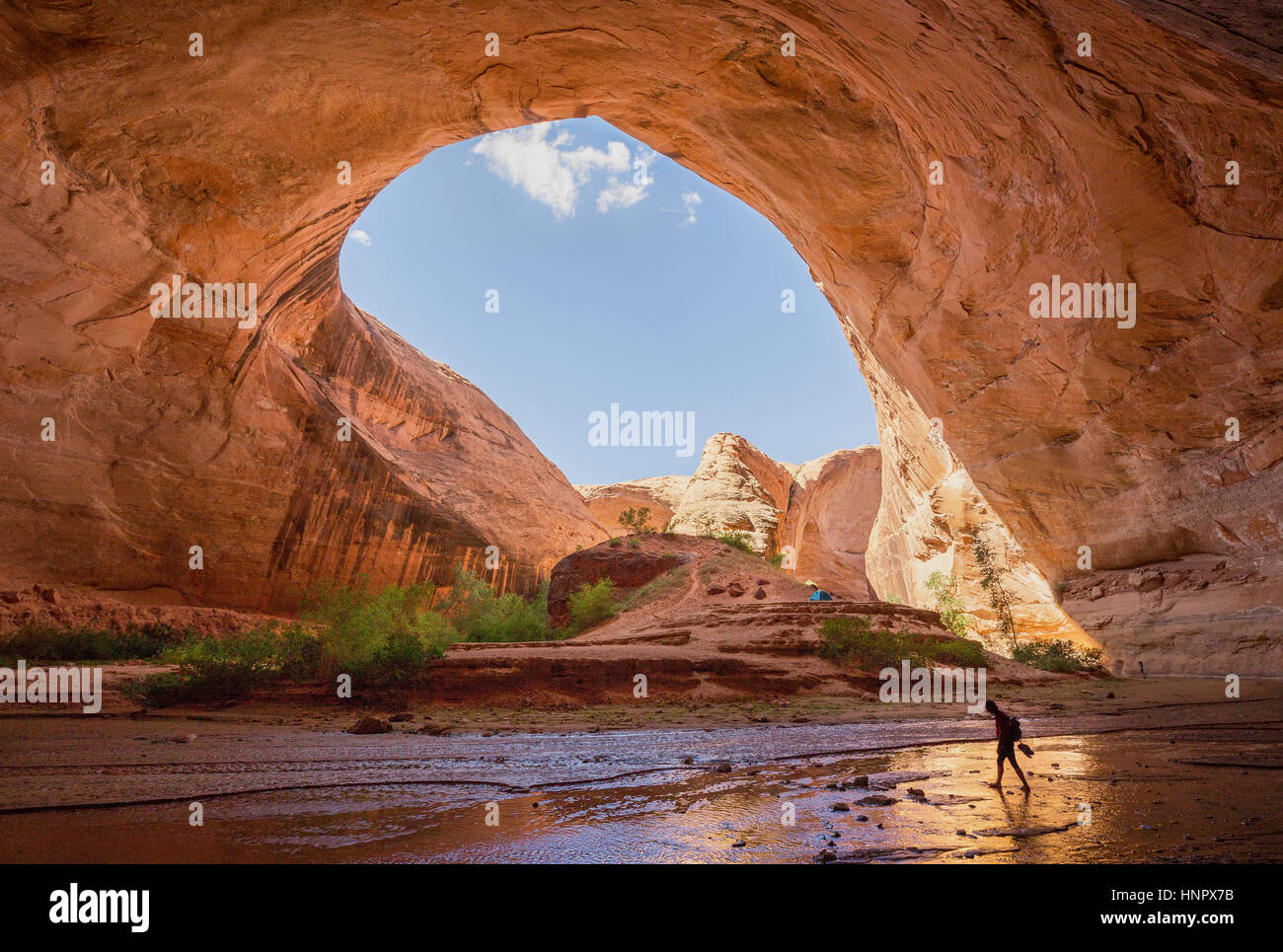 Ampio angolo di visione dei maschi di escursionista backpacking sotto Jacob Hamblin Arch in Coyote Gulch in una giornata di sole con cielo blu, la grande scala Escalante, Utah, USA Foto Stock