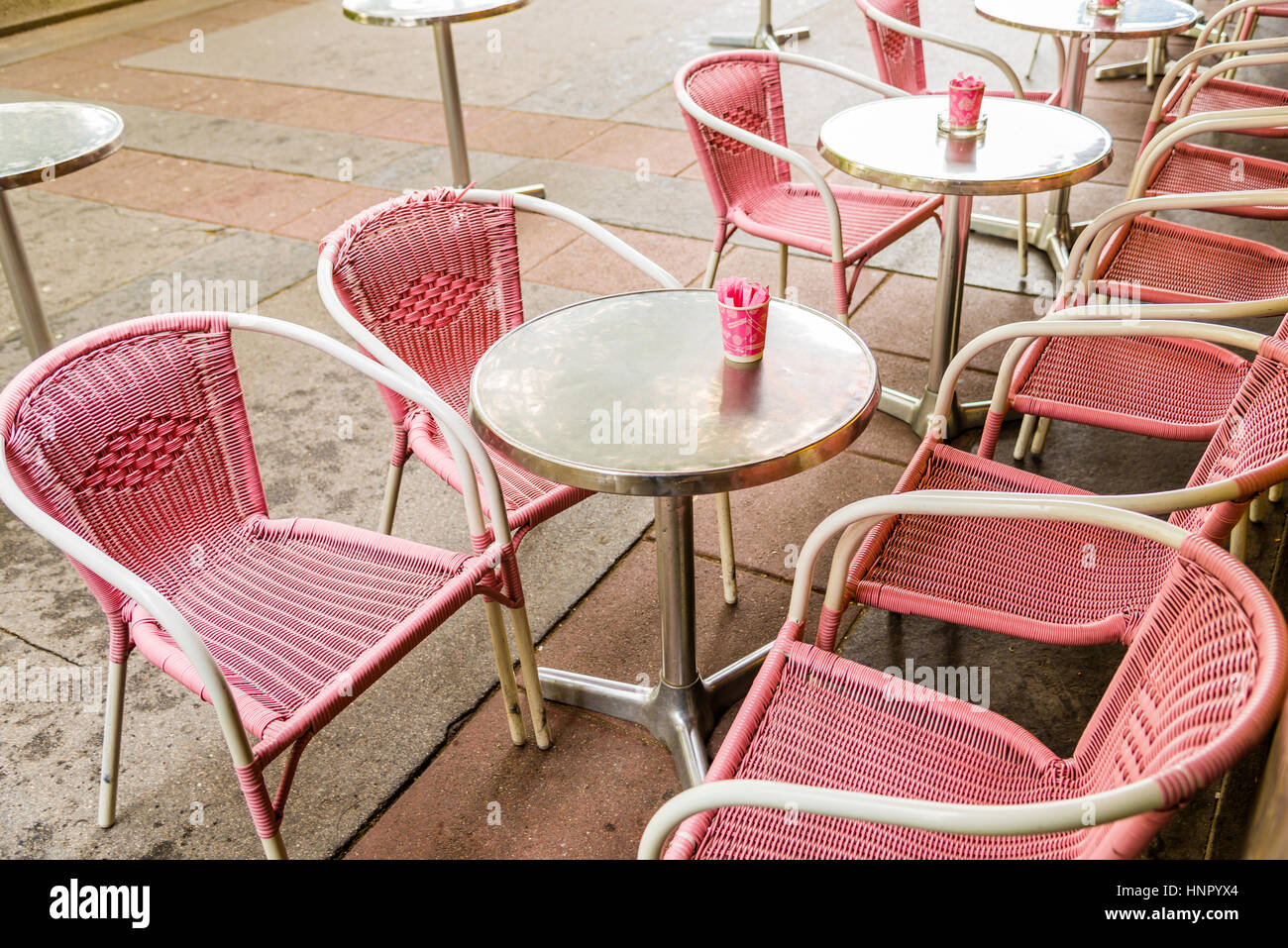 Rosa di plastica sedie di vimini e rotonde Tavole in argento con rosa bicchieri contenenti zucchero al di fuori di un bistro. Foto Stock