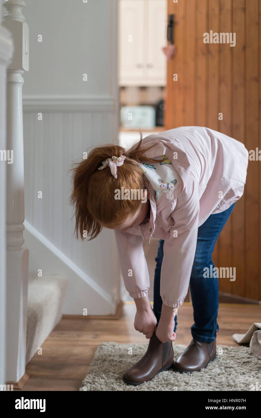 Una bambina mettendo i suoi stivali su pronto a lasciare la casa. Foto Stock