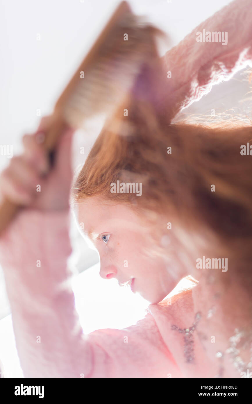 Una bambina spazzolando i suoi capelli rossi. Foto Stock