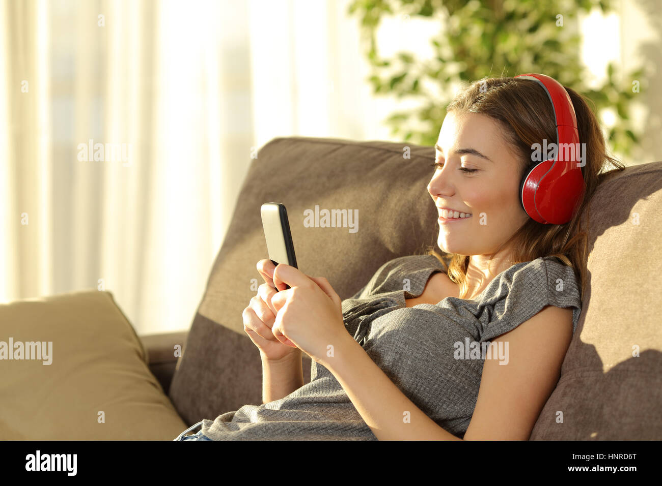 Single teen ascoltare musica on line con uno smart phone e cuffie seduto su un divano n il salotto di casa Foto Stock