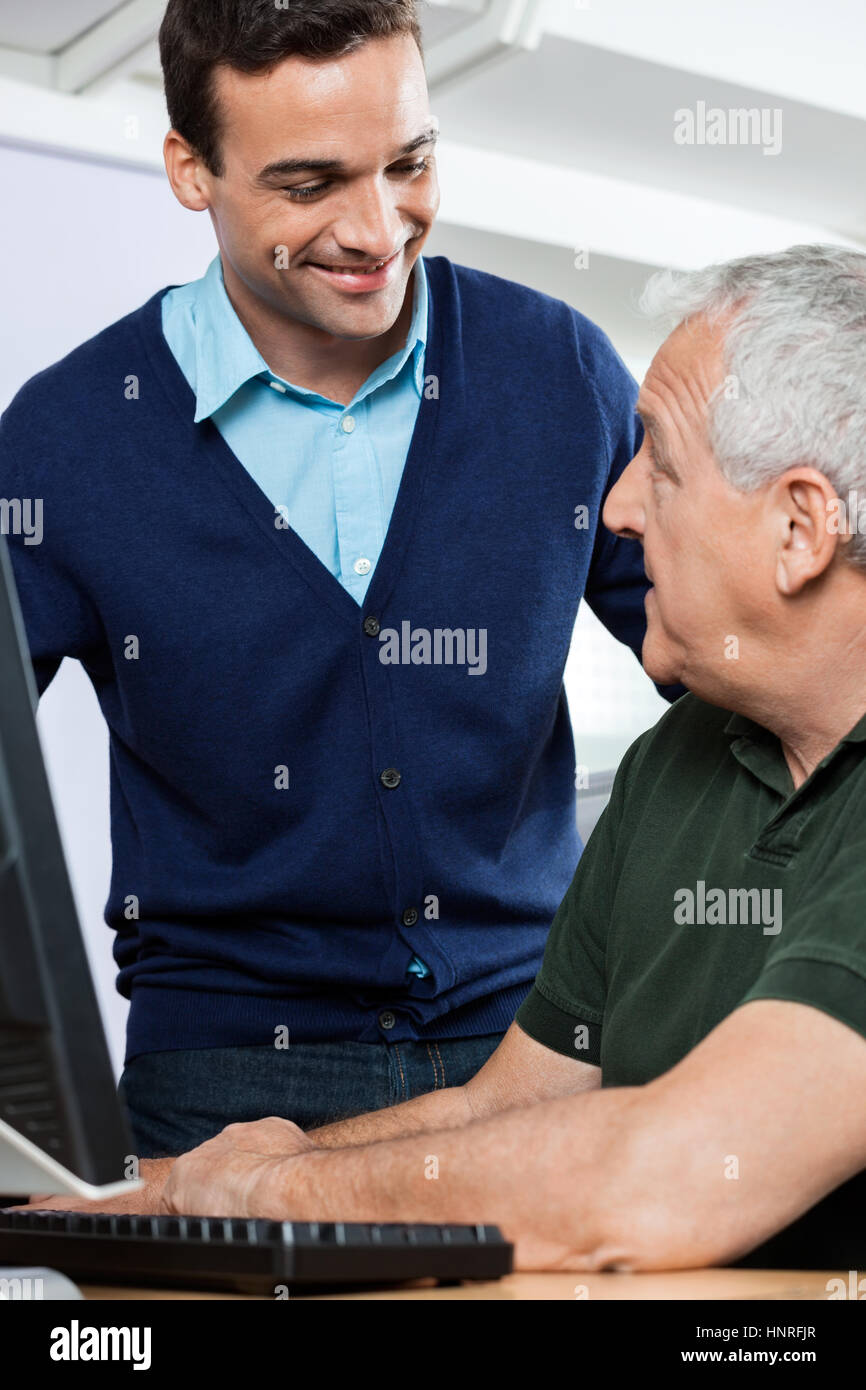 Il tutor sorridente guardando anziano studente in classe computer Foto Stock