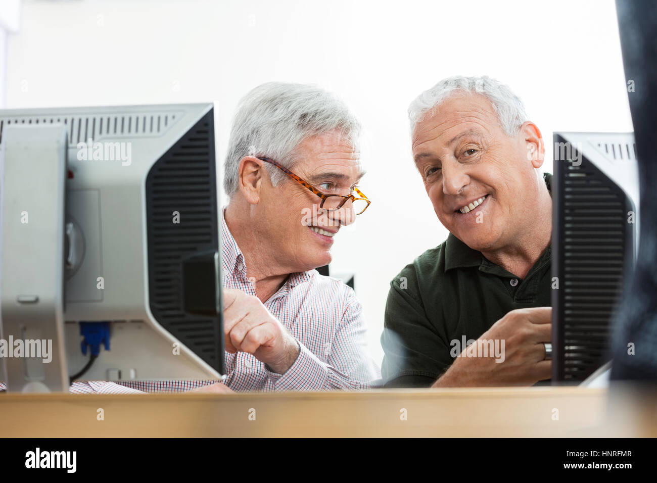 Felice l'uomo anziano con il compagno seduto alla scrivania del computer Foto Stock