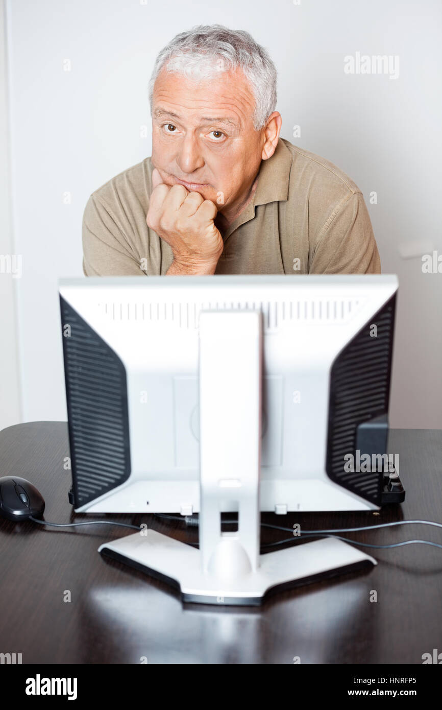 Grave senior uomo seduto alla scrivania del computer in classe Foto Stock
