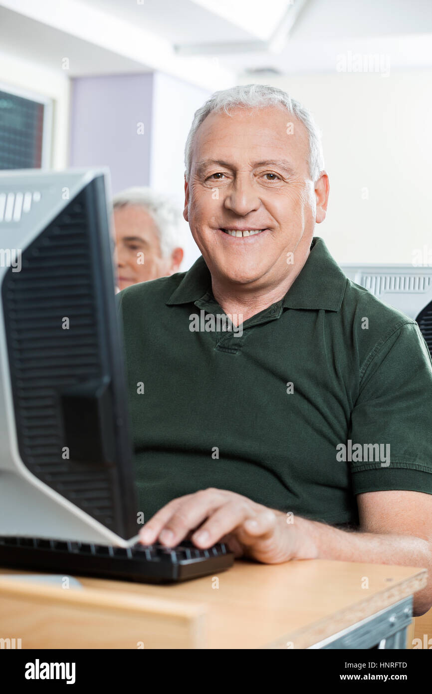 Felice senior uomo seduto in aula computer Foto Stock