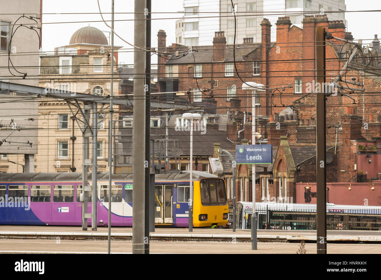 Leeds cityscape. Stazione ferroviaria di Leeds stazione ferroviaria piattaforma con fili di overhead,e alloggiamento tipiche e stili di costruzione dietro Foto Stock