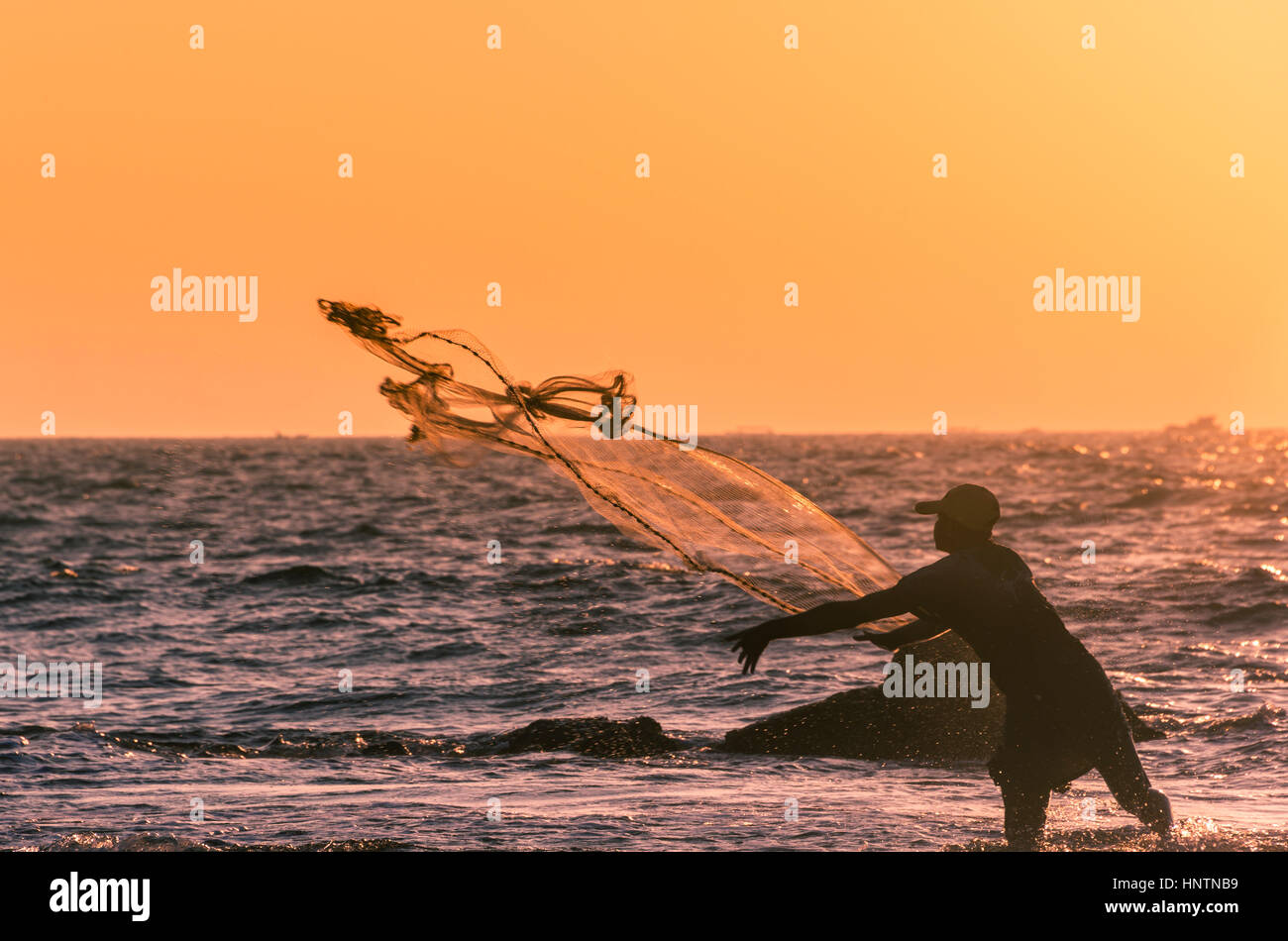 Pescatore locale getta la pesca net, retroilluminato, tramonto, Chaung Thar Beach, la baia del Bengala, Ayeyarwady, Myanmar Foto Stock